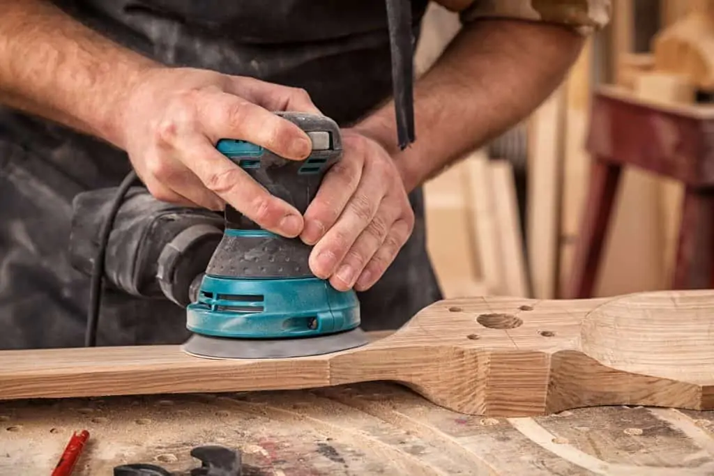 Using a random orbital sander to sand a piece of wood furniture.